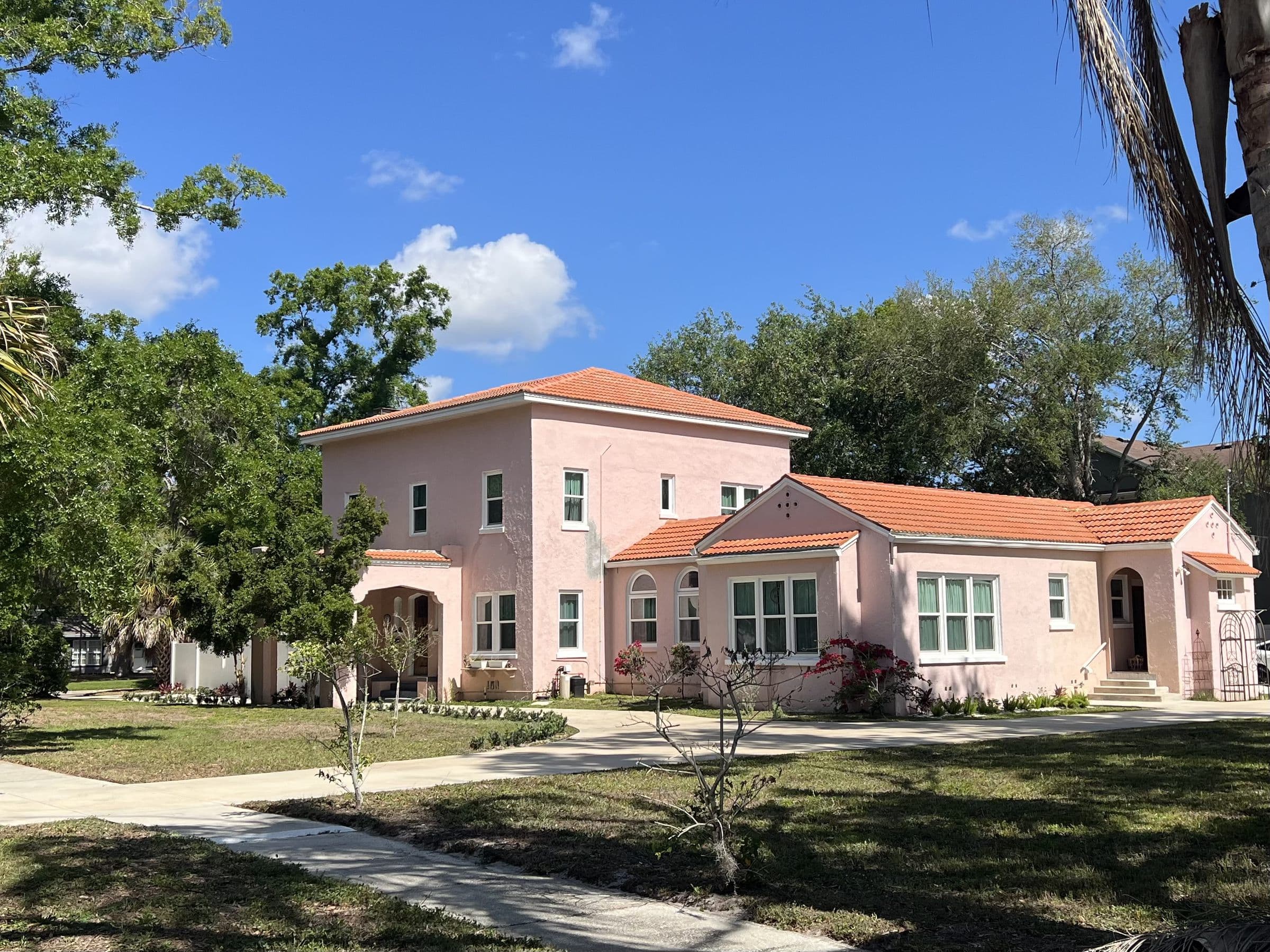 A 1920s stucco house with an orange tile roof and a wide front lawn under a blue sky in Oldsmar, Florida